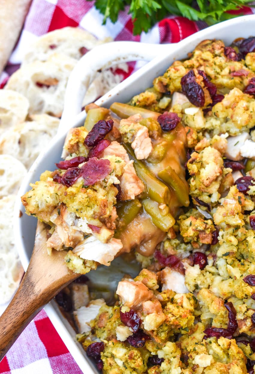 a wooden spoon scooping thanksgiving casserole out of a white baking dish