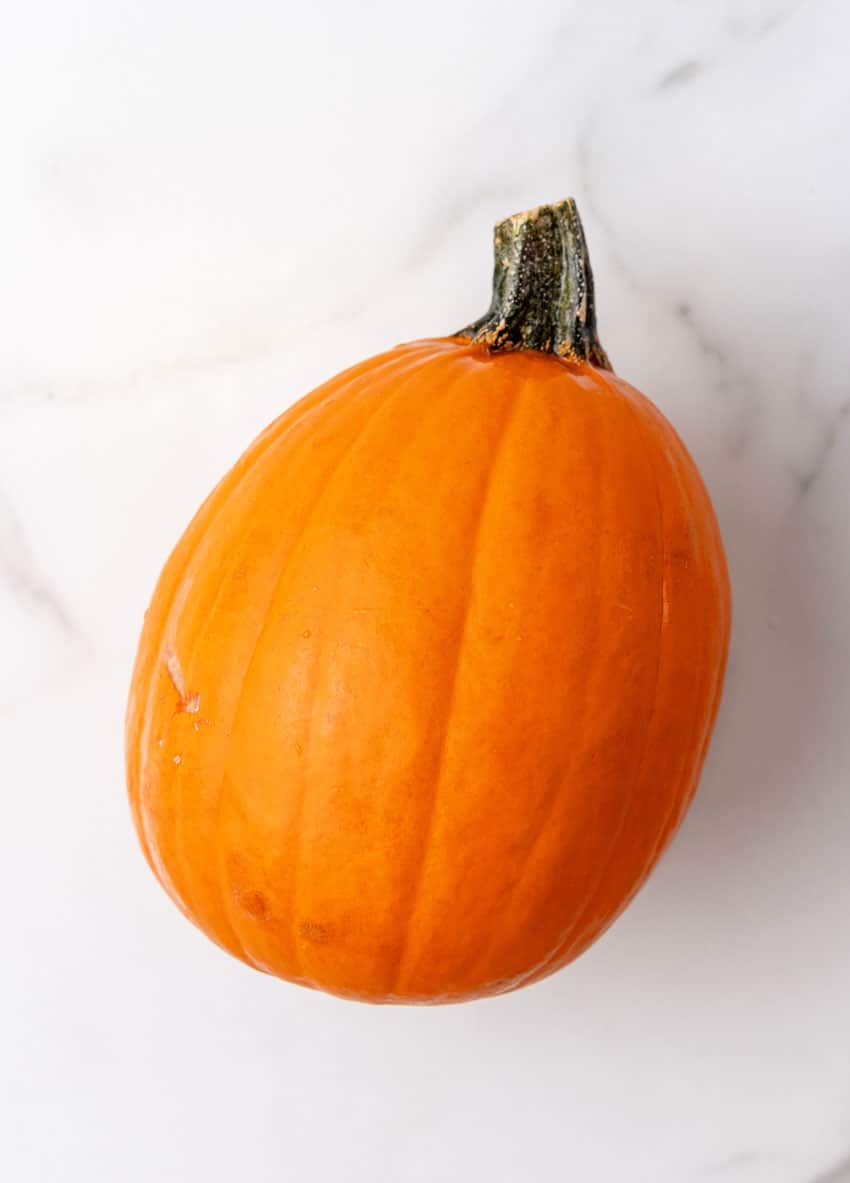 an overhead image showing a close up of a ripe pie pumpkin on a marble countertop