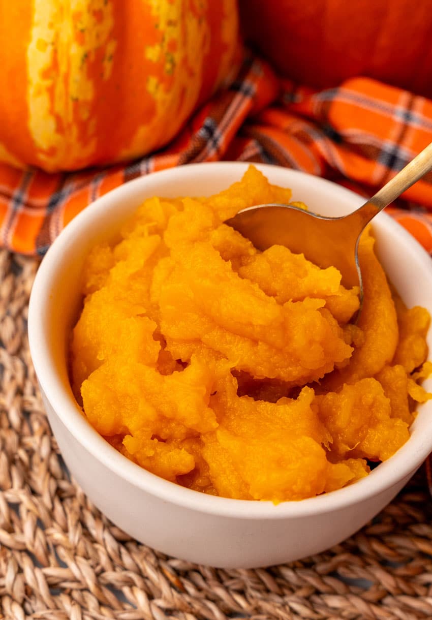 a gold spoon scooping instant pot pumpkin puree out of a small white bowl
