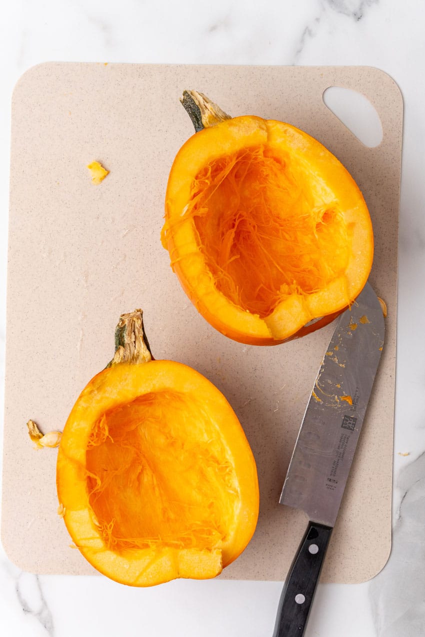 two hollowed out halves of a ripe pie pumpkin on a plastic cutting board
