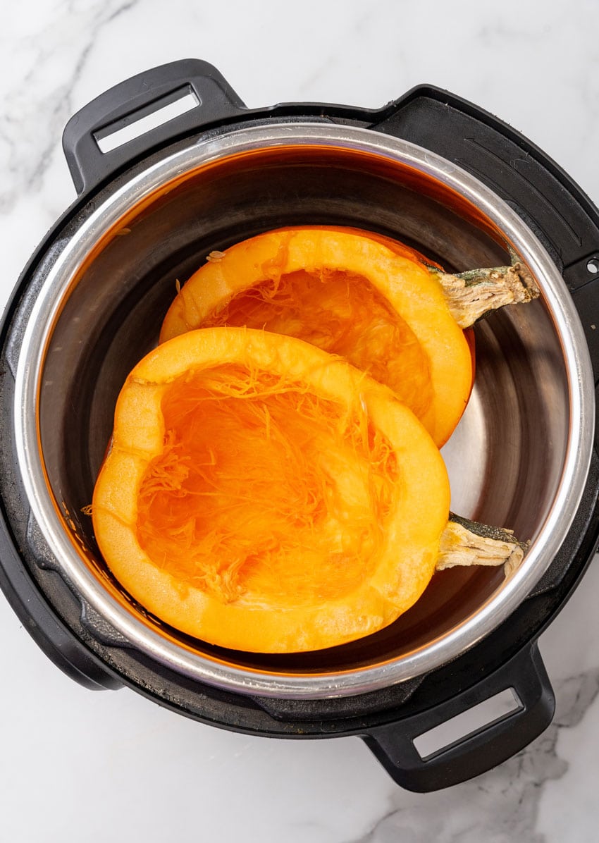 two hollowed out halved of a pie pumpkin in the bowl of an instant pot
