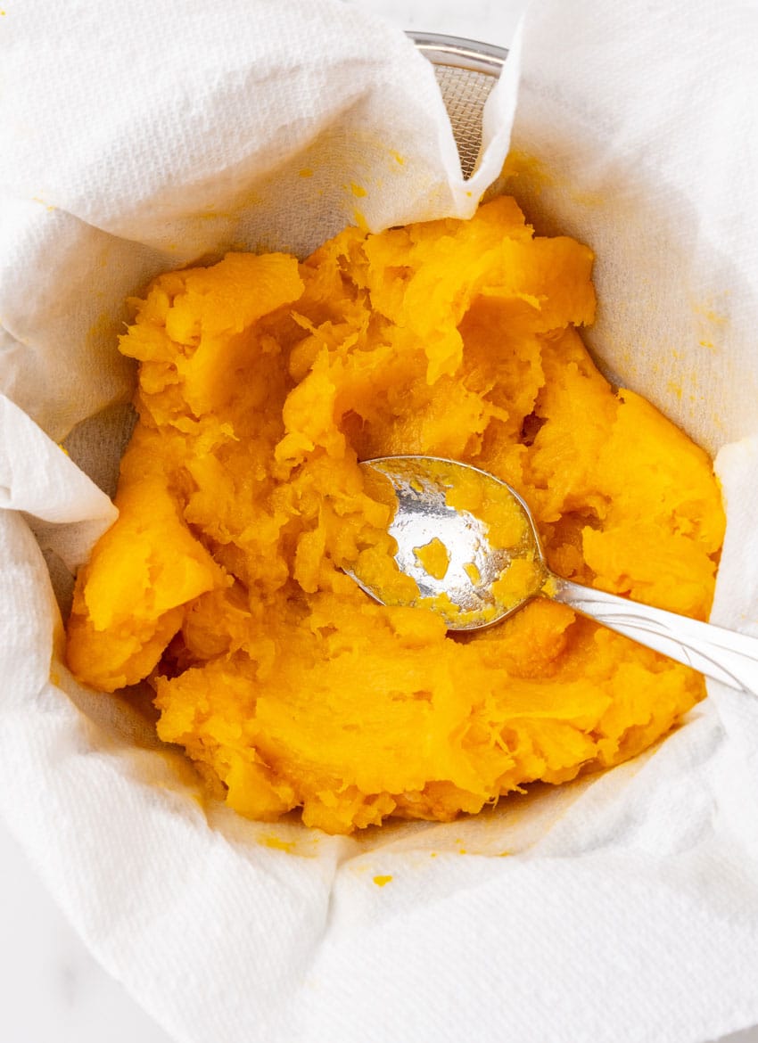 roasted pumpkin being pressed through a cheesecloth with a silver spoon