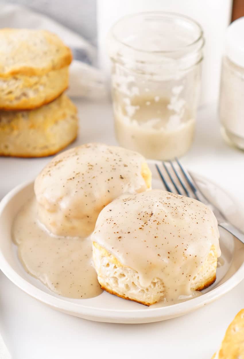 homemade white gravy over two fluffy biscuits on a white plate
