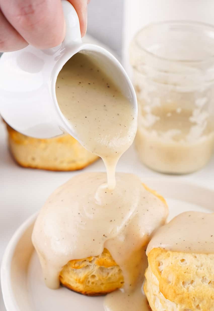 easy country gravy being poured over two fluffy white biscuits on a white plate