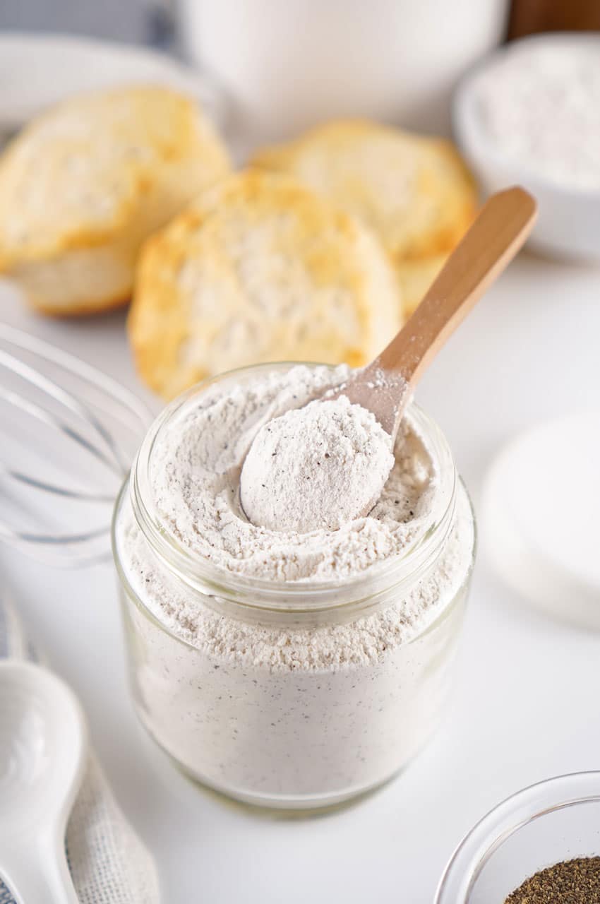 a small wooden spoon scooping homemade white gravy mix out of a small glass jar
