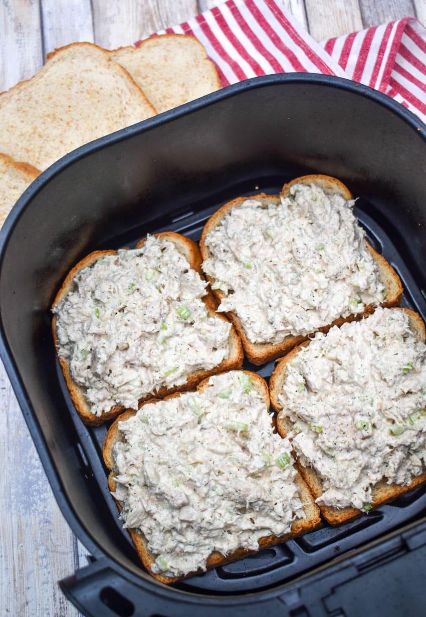 tuna salad topped slices of bread in the basket of an air fryer