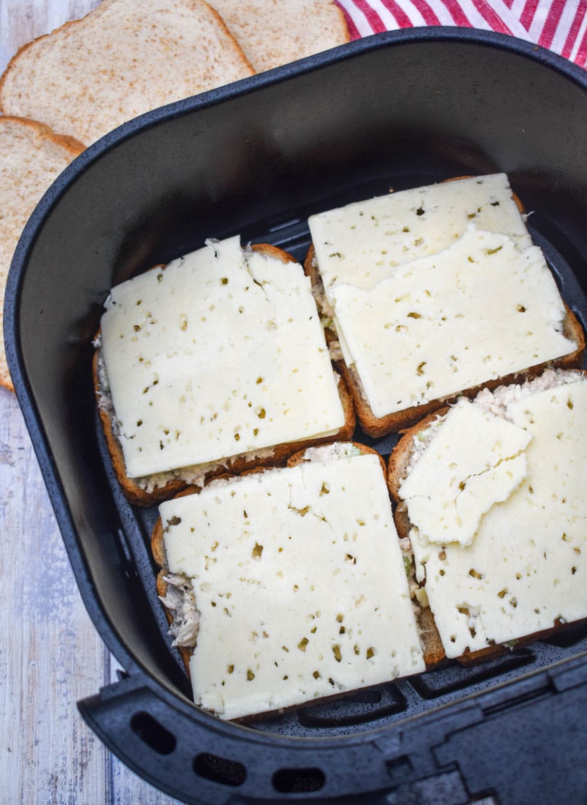 slices of havarti cheese over tuna salad sandwiches in the basket of an air fryer