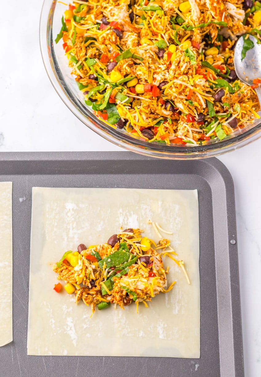 an eggroll wrapper topped with southwestern chicken and vegetable filling on a metal baking sheet