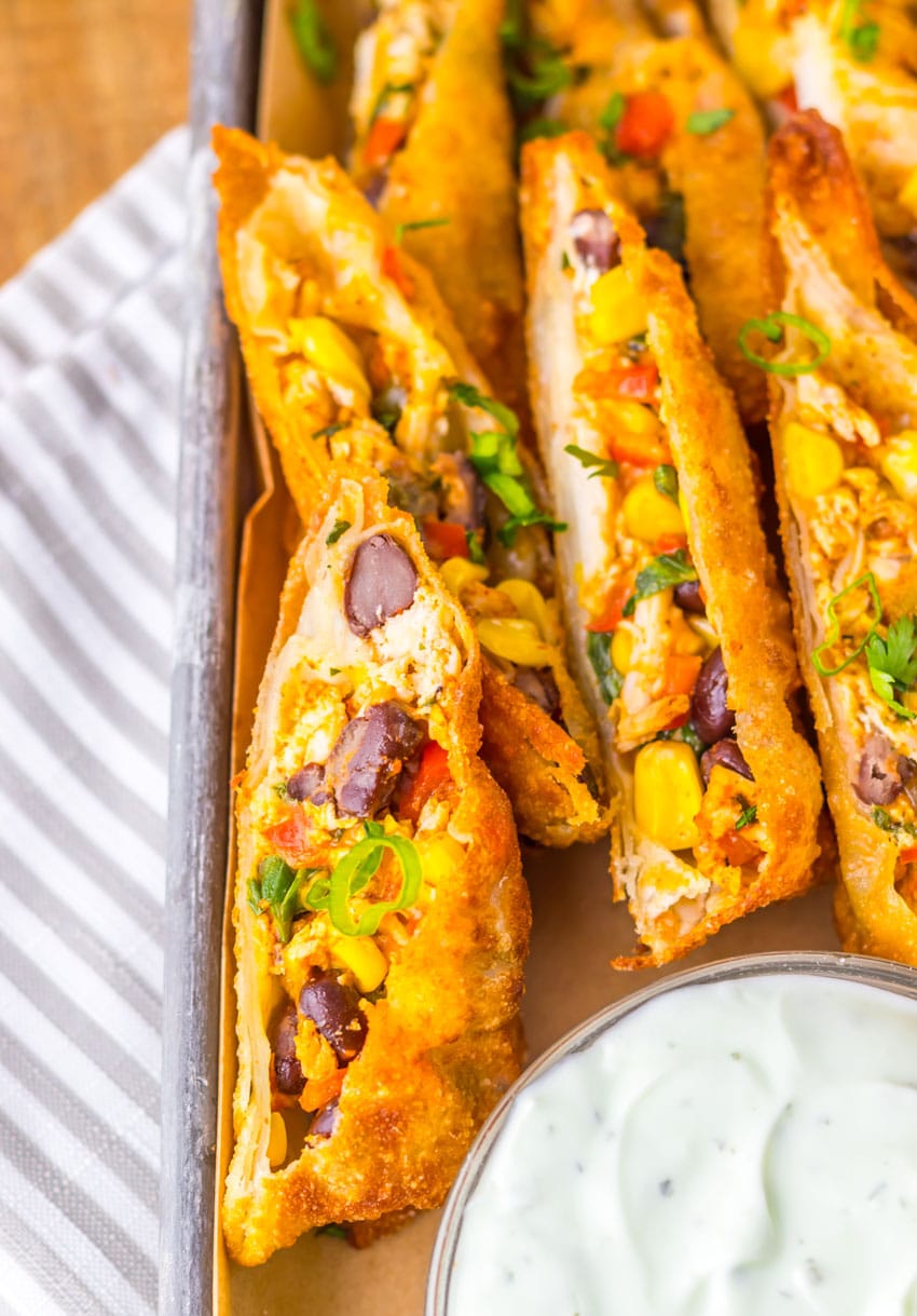 cut southwestern egg rolls on a metal tray with a glass bowl of cilantro sour cream on the side