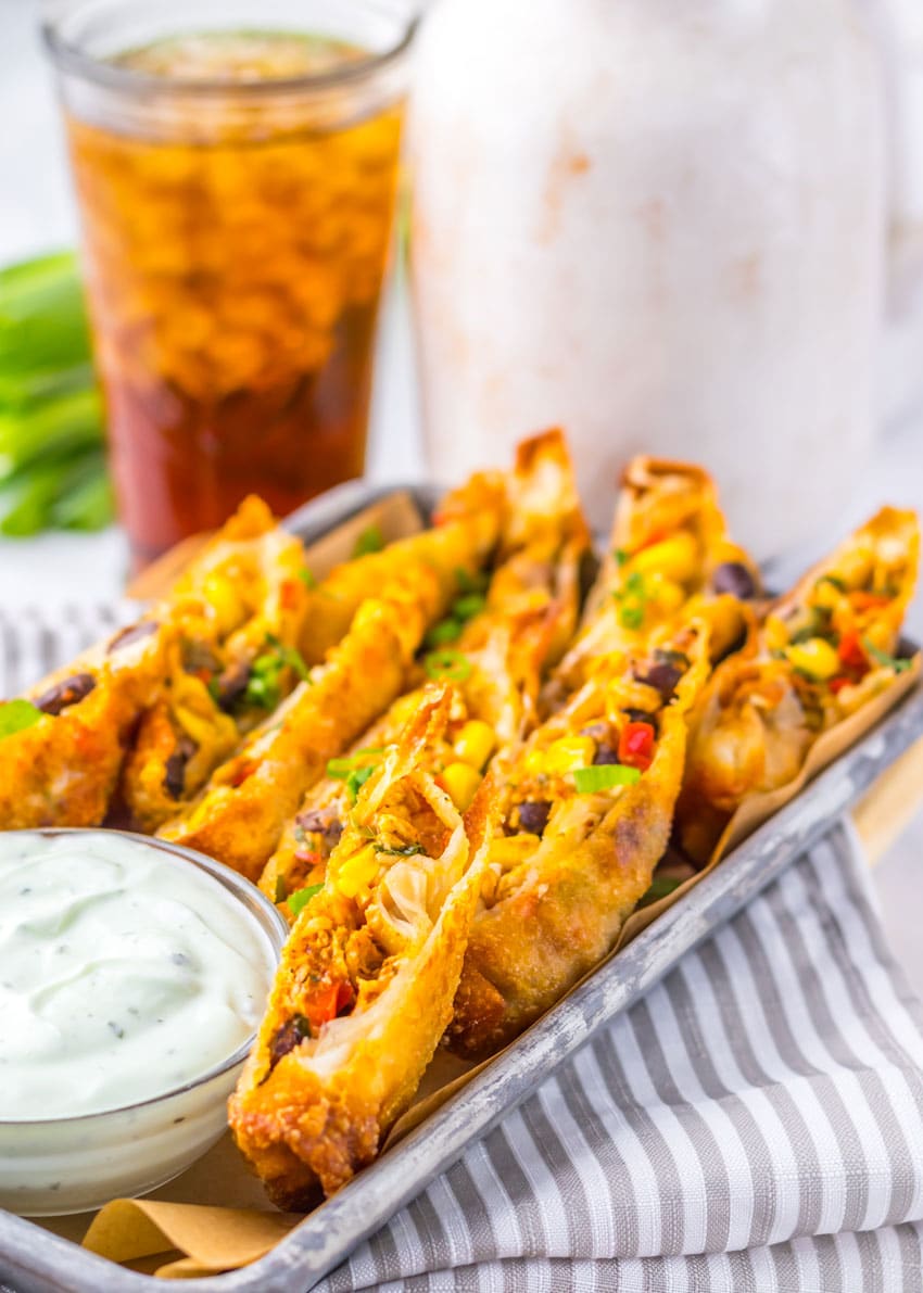 cut southwestern egg rolls on a metal tray with a glass bowl of cilantro sour cream on the side