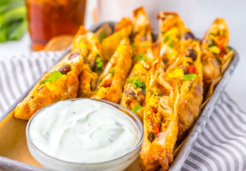 cut southwestern egg rolls on a metal tray with a glass bowl of cilantro sour cream on the side