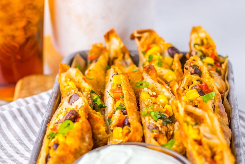 cut southwestern egg rolls on a metal tray with a glass bowl of cilantro sour cream on the side