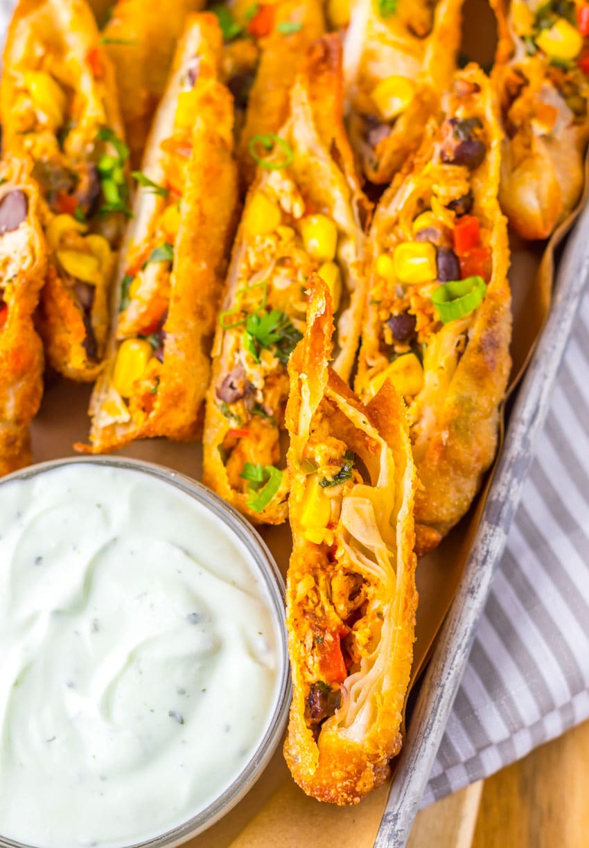 cut southwestern egg rolls on a metal tray with a glass bowl of cilantro sour cream on the side