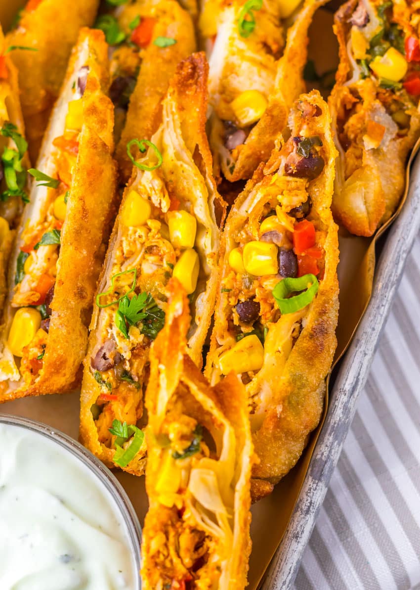 cut southwestern egg rolls on a metal tray with a glass bowl of cilantro sour cream on the side