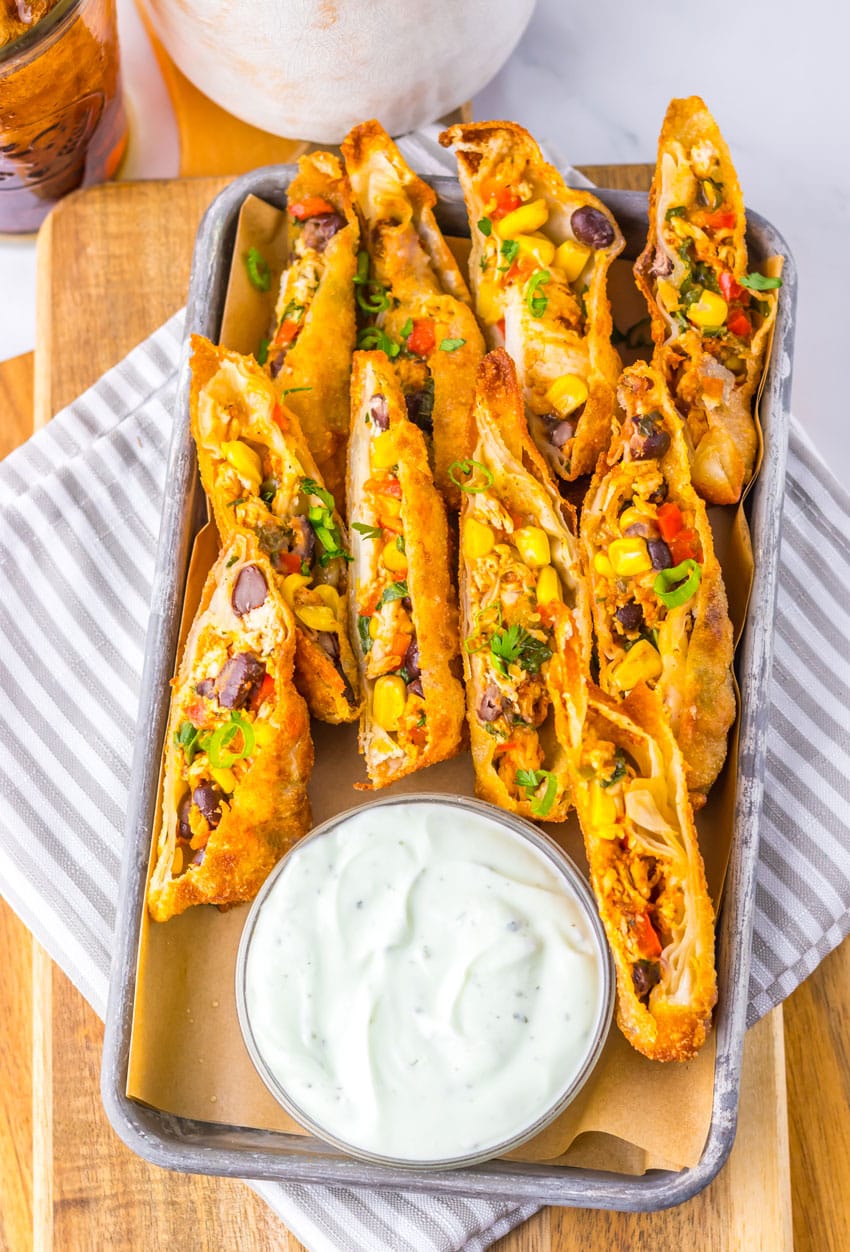 cut southwestern egg rolls on a metal tray with a glass bowl of cilantro sour cream on the side