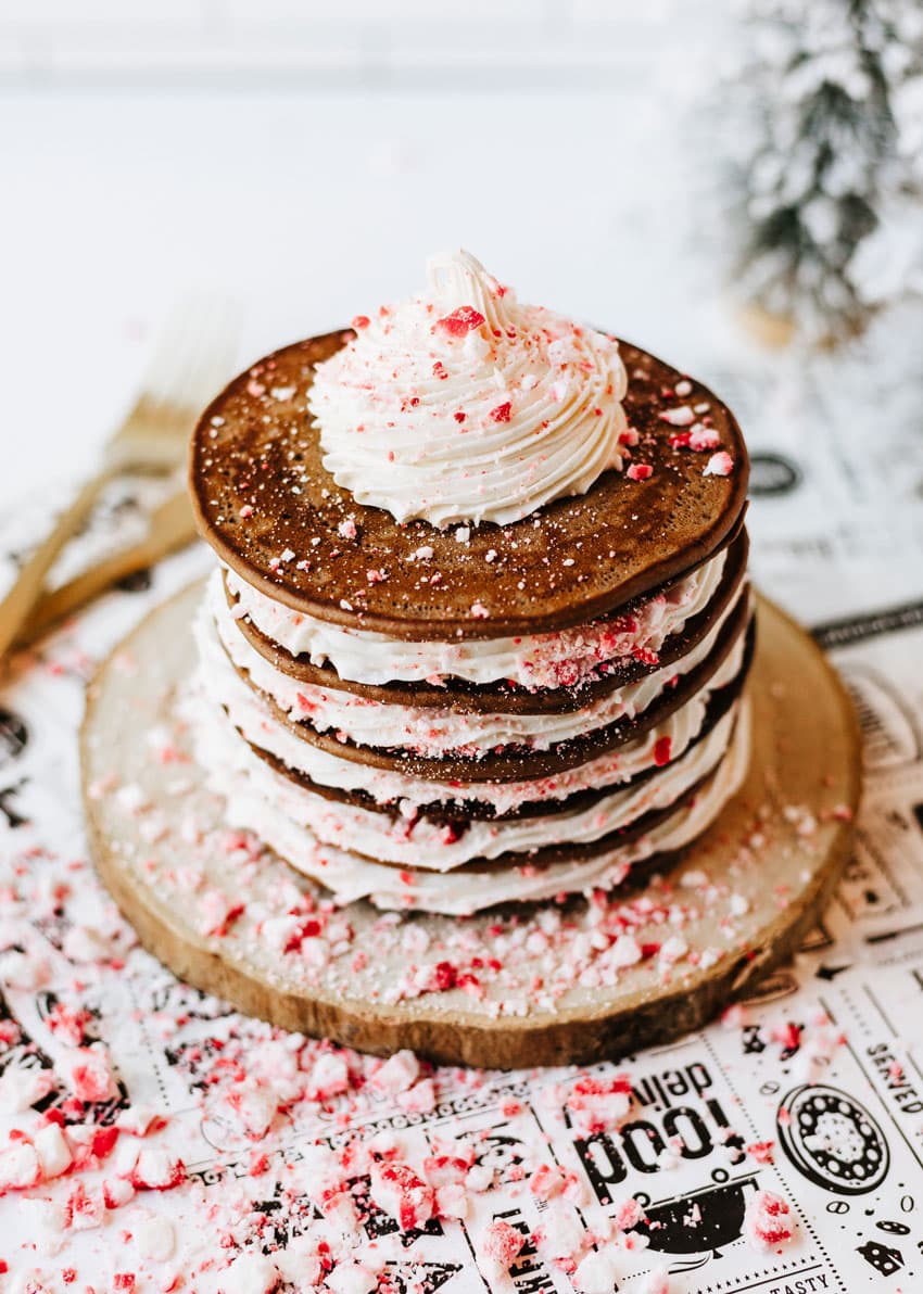 a stack of peppermint pancakes on a wooden cutting board surrounded by peppermint candy pieces