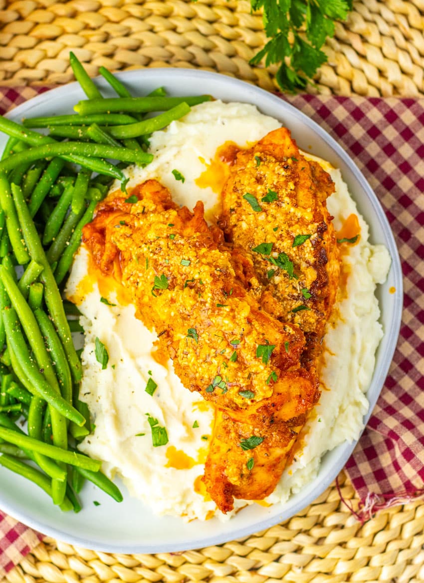 garlic parmesan baked chicken over mashed potatoes on a gray plate