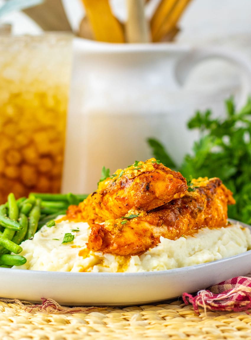 garlic parmesan baked chicken over mashed potatoes on a gray plate with green beans on the side