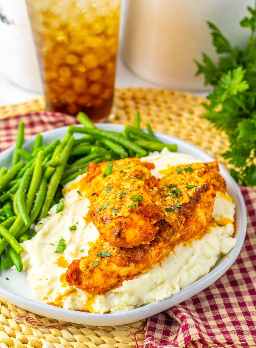 garlic parmesan baked chicken over mashed potatoes on a gray plate with green beans on the side