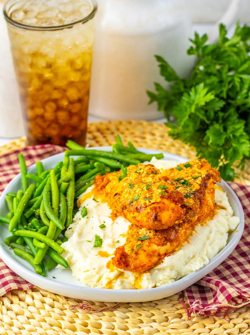 garlic parmesan baked chicken over mashed potatoes on a gray plate with green beans on the side