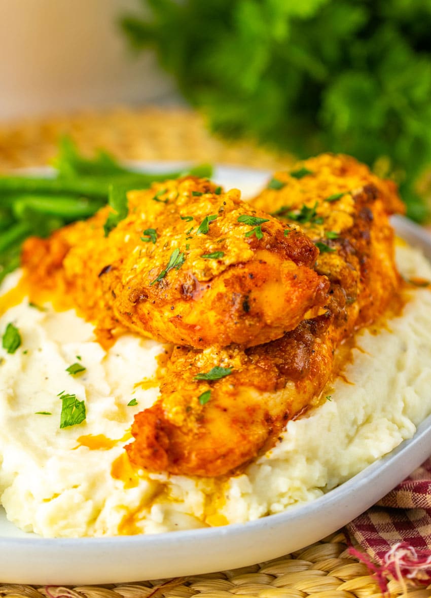 garlic parmesan baked chicken over mashed potatoes on a gray plate