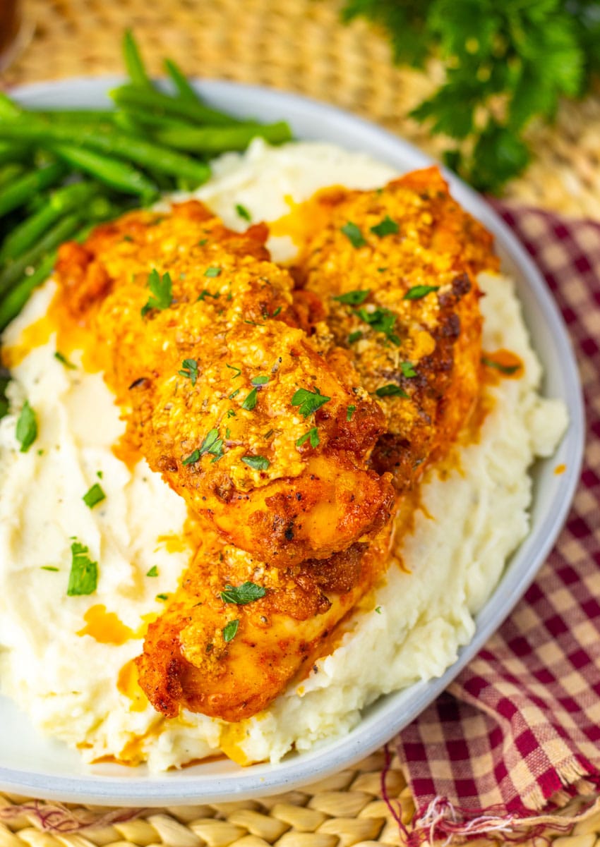 garlic parmesan baked chicken over mashed potatoes on a gray plate