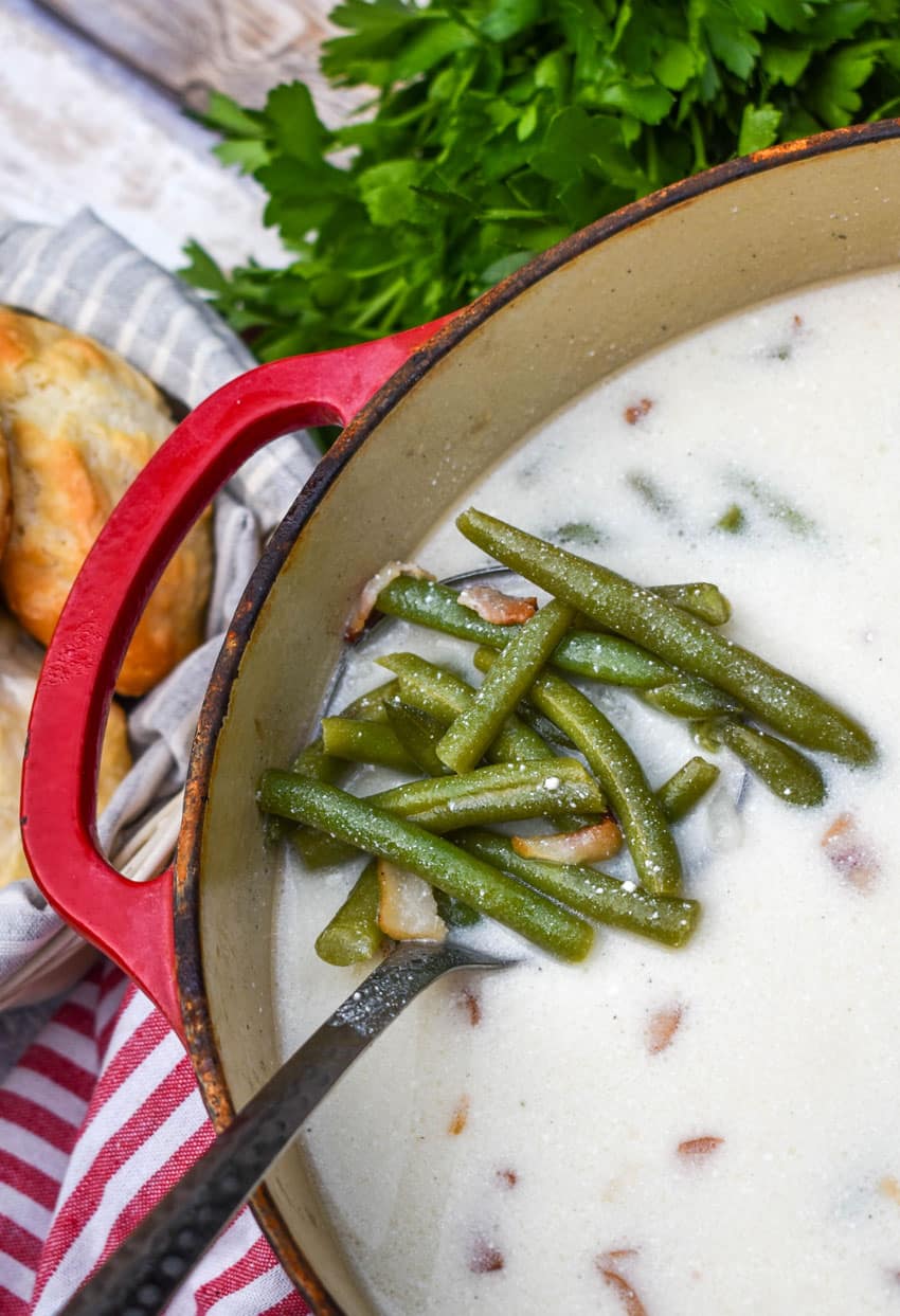 a silver ladle scooping green bean soup out of a red dutch oven