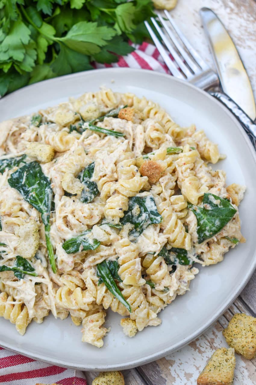 slow cooker chicken caesar pasta on a gray plate with fresh herbs in the background