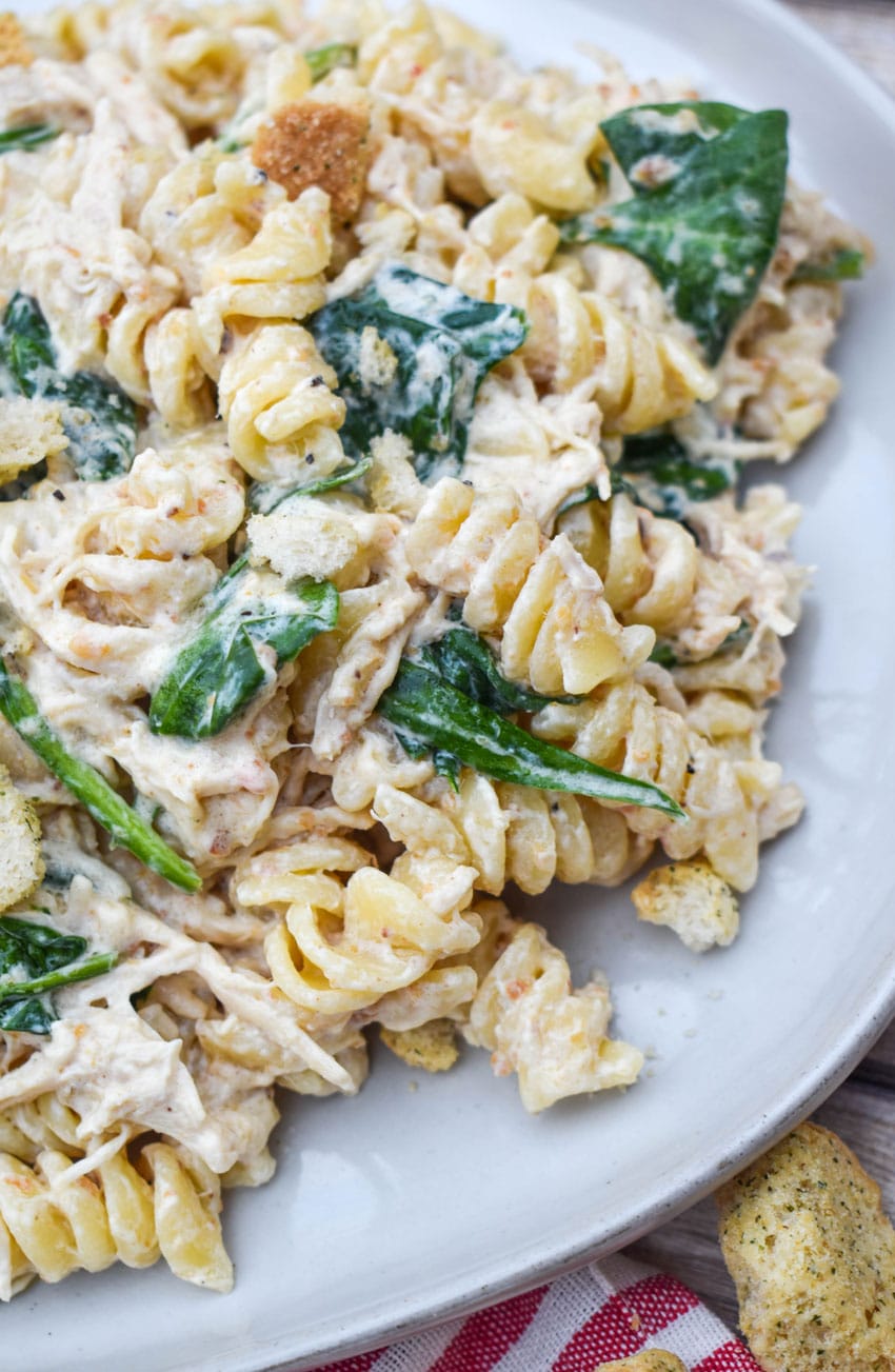 slow cooker chicken caesar pasta on a gray plate with fresh herbs in the background