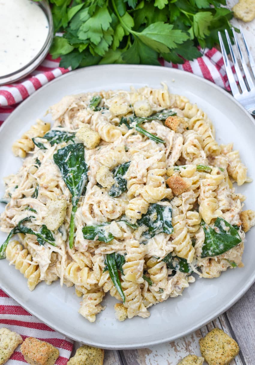 slow cooker chicken caesar pasta on a gray plate with fresh herbs in the background