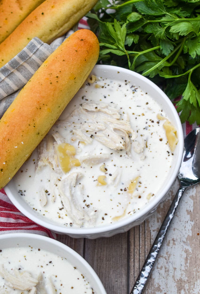 WHITE LASAGNA SOUP IN A WHITE BOWL WITH A BREADSTICK RESTING ON THE SIDE