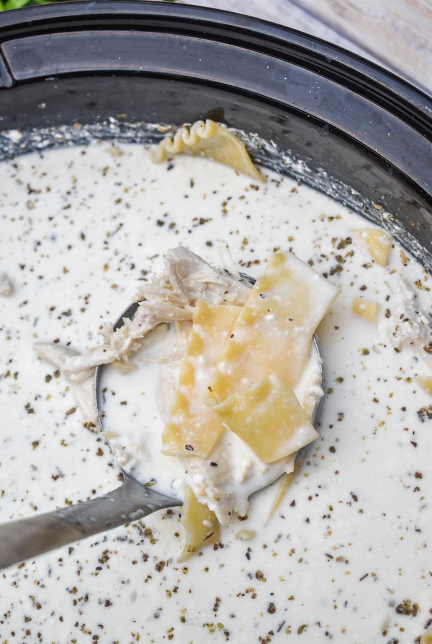 a silver ladle scooping white lasagna soup out of a black slow cooker