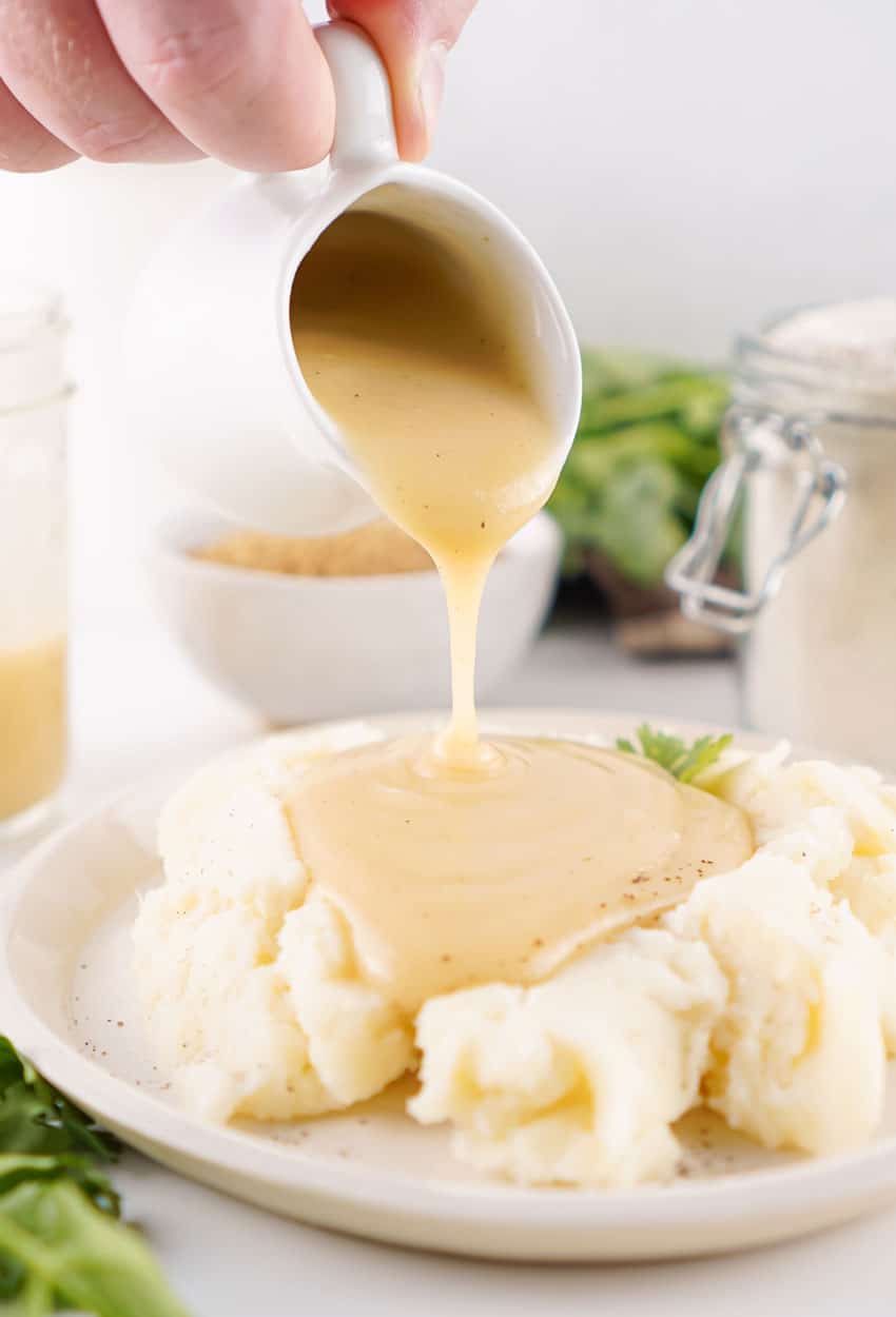homemade brown gravy mix being poured over mashed potatoes on a white plate