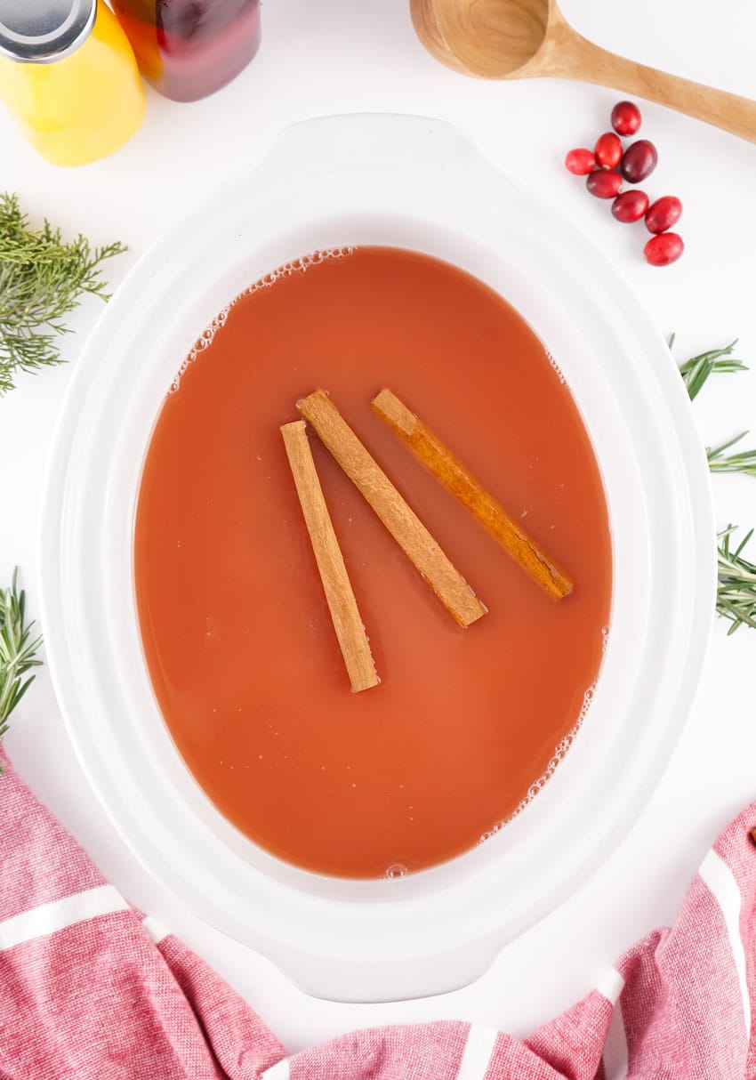 hot christmas punch with cinnamon sticks floating on top in a white crockpot