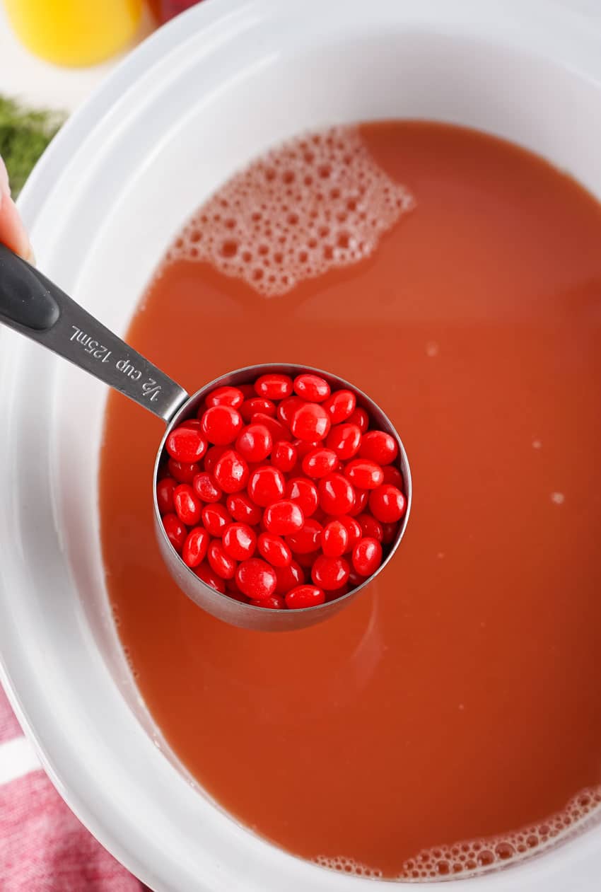red hot candies in a small measuring cup held over a white crockpot