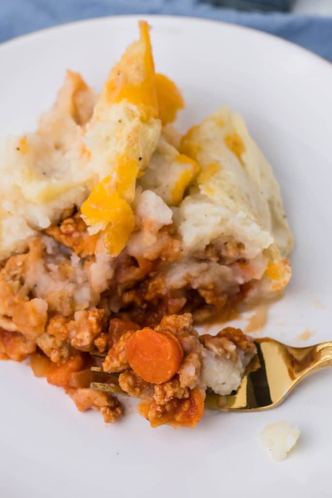 buffalo chicken shepherd's pie on a white dinner plate with a golden fork