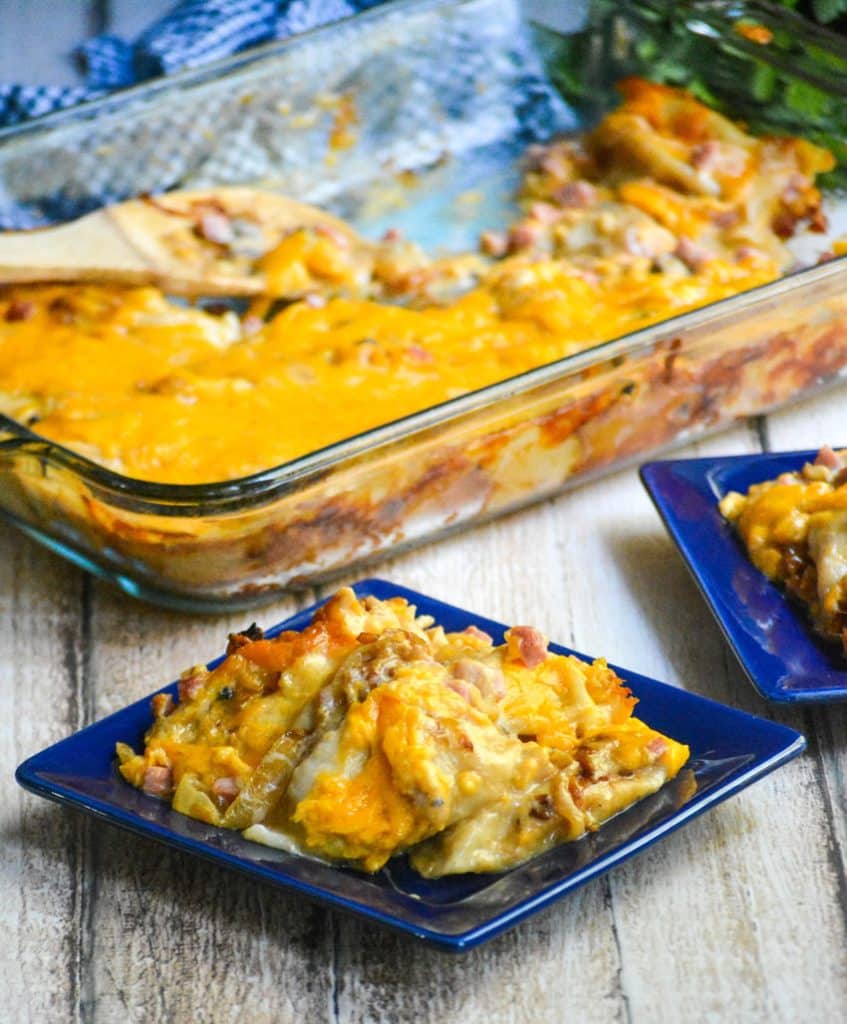 cheesy ham & pierogi casserole served on small square blue plates in front of the casserole dish