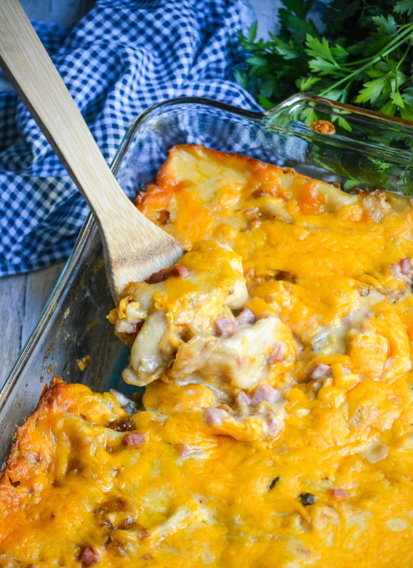 a wooden spoon scooping into a cheesy ham and pierogi casserole