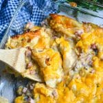 a wooden spoon scooping into a cheesy ham and pierogi casserole