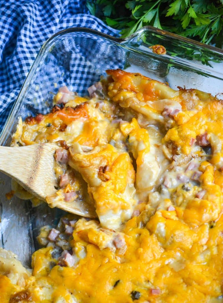 a wooden spoon scooping into a cheesy ham and pierogi casserole