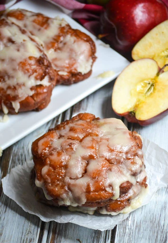 powdered sugar glazed fried apple fritters on a parchment paper square