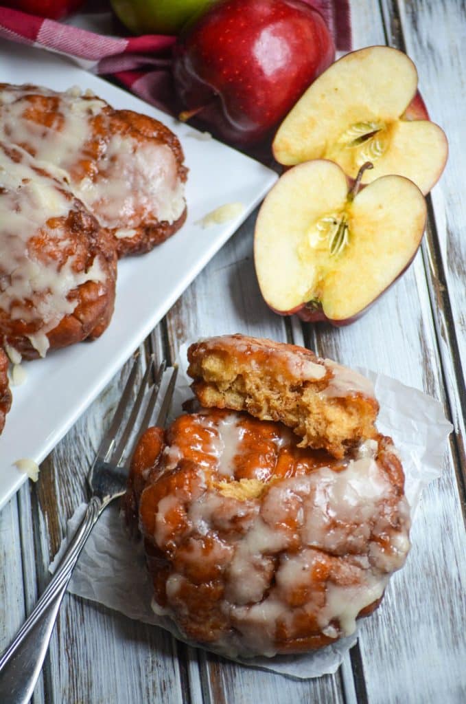 powdered sugar glazed fried apple fritters on a parchment paper square