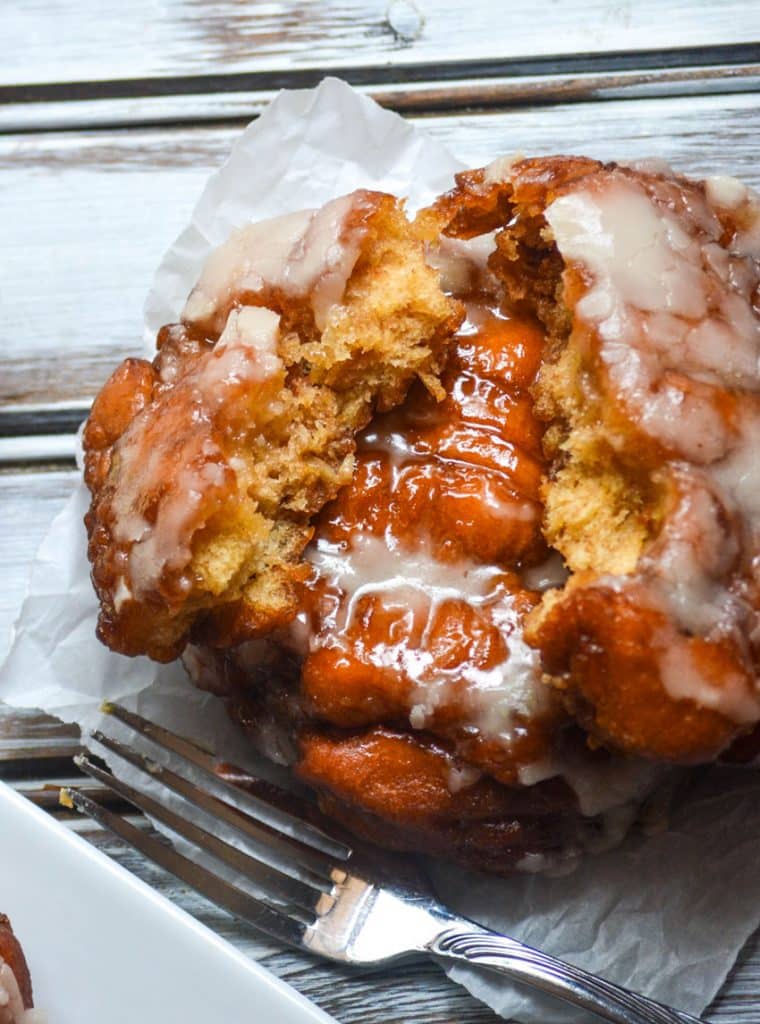 glazed fried apple fritters stacked on a parchment paper square