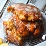 glazed apple fritters stacked on a parchment paper square