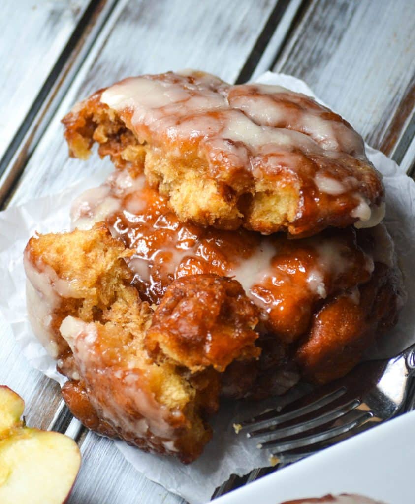 glazed apple fritters stacked on a parchment paper square