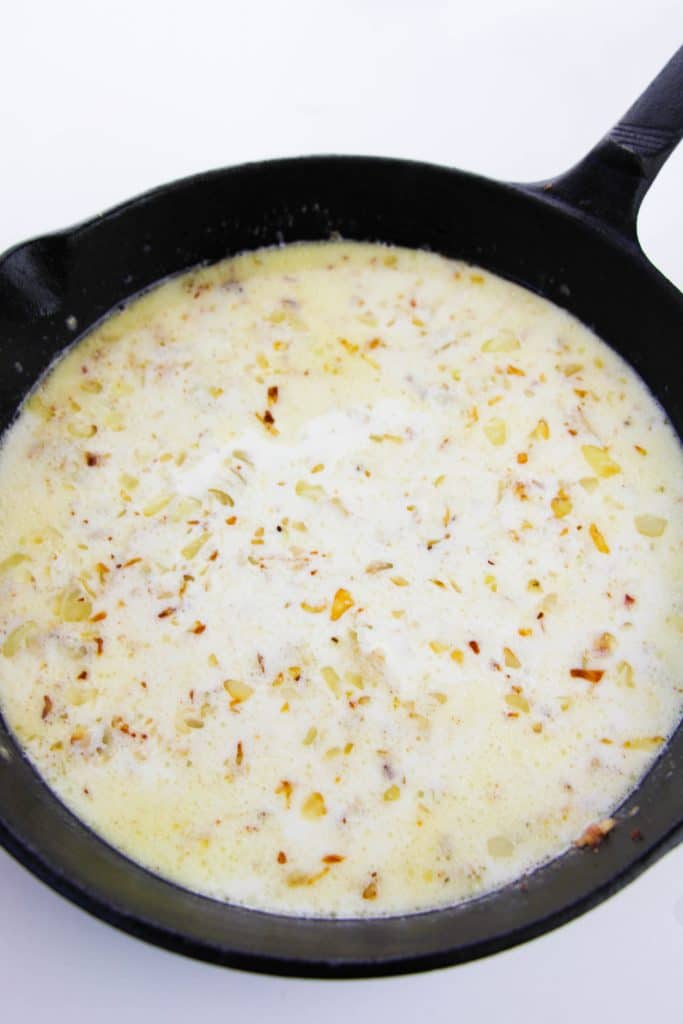 sauteed onions mixed with broth and cream in a cast iron skillet