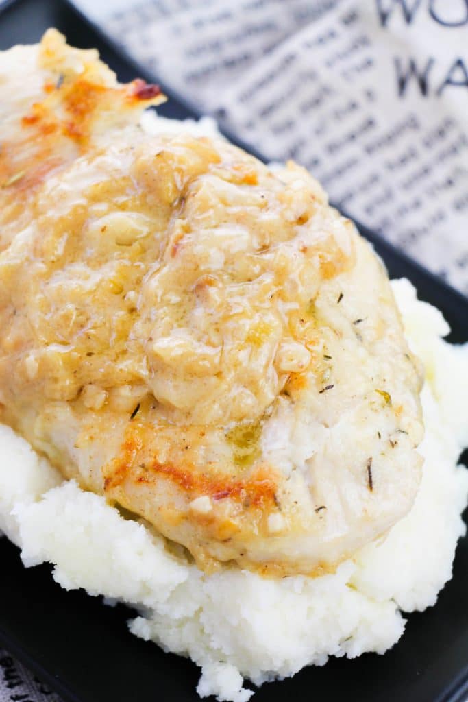 a smothered chicken breast served over a bed of fluffy white mashed potatoes