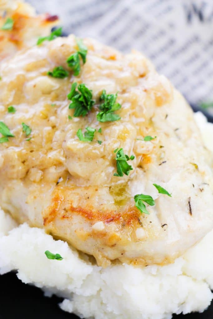 smothered skillet chicken breasts topped with fresh parsley leaves on a bed of mashed potatoes