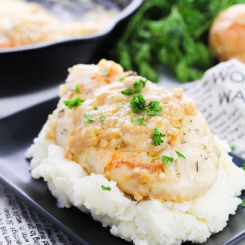 smothered skillet chicken breasts topped with fresh parsley leaves on a bed of mashed potatoes