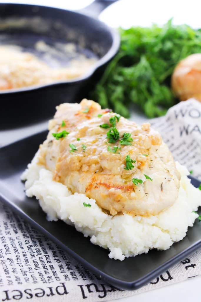 smothered skillet chicken breasts topped with fresh parsley leaves on a bed of mashed potatoes